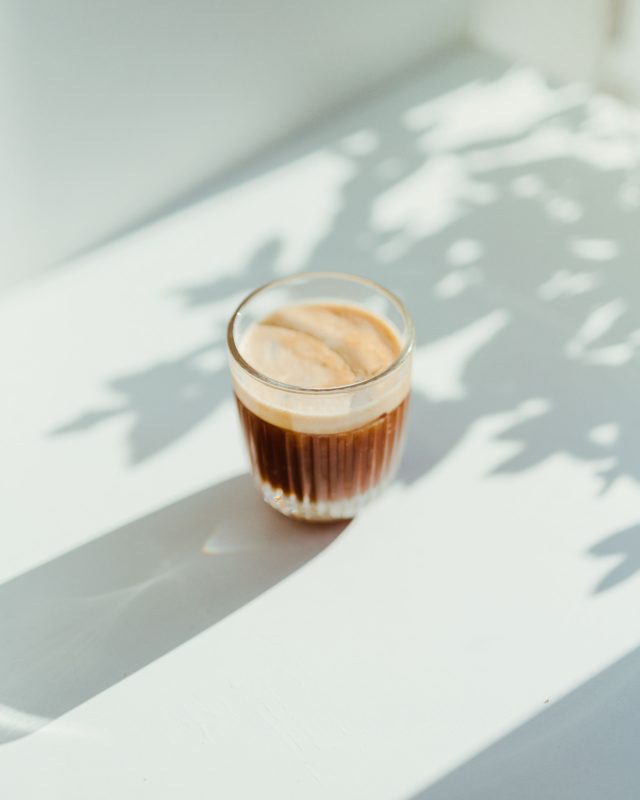 Ein Glas Milchkaffee mit Schaum auf einer Fensterbank zur Illustration des Themas Stillen und Kaffee.