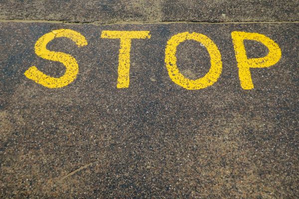 Das Wort "Stop" in gelben Großbuchstaben auf Asphalt gemalt, als Symbol für Stillhindernisse, bei denen Stillen kontraindiziert ist.