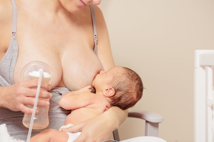 Eine Mutter stillt ihr Baby an der linken Brust und pumpt gleichzeitig an der rechten Brust. 